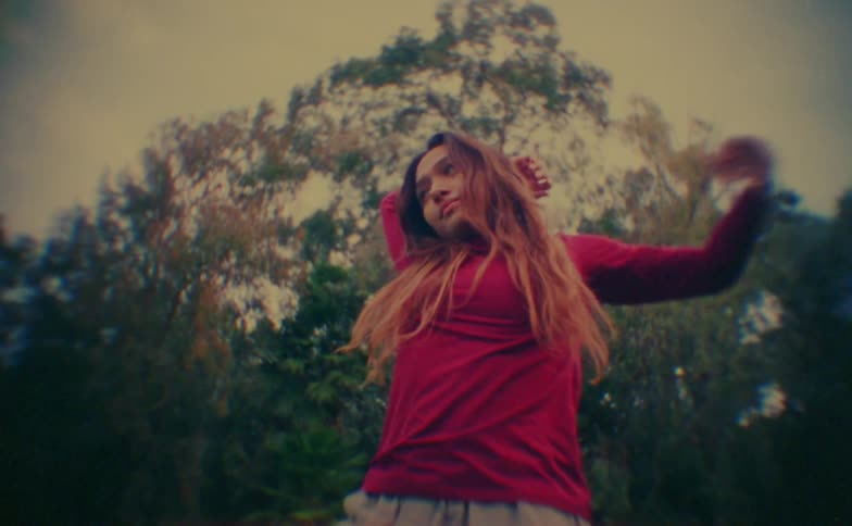 A young girl in a red shirt dances in the woods her long hair moving with her steps as tall trees form a natural backdrop around her
