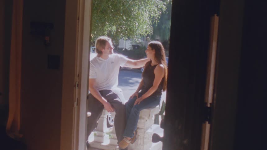 Young adult man and young adult woman sitting down and kissing on a porch of a house on a suburban area outdoors during day time