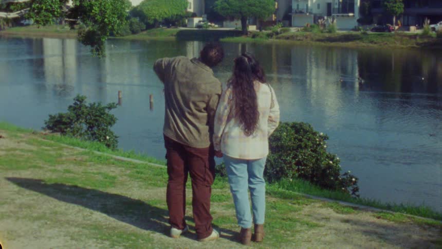 Couple stands side by side by an urban lake with one person pointing toward the horizon