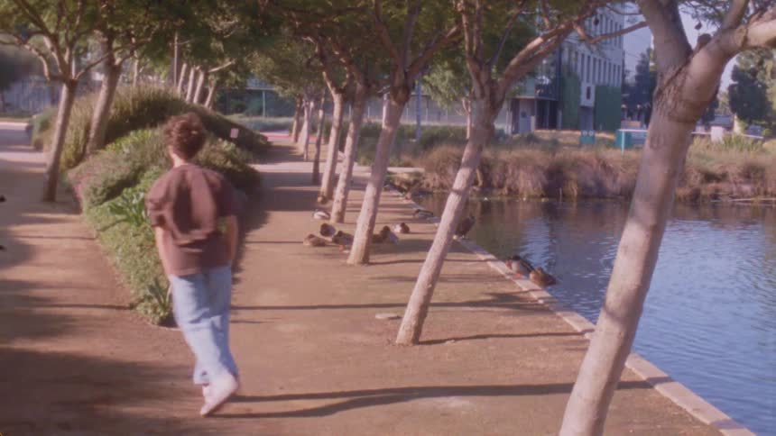 A teenage male dancer dancing outdoors by a pond in an urban city during daytime