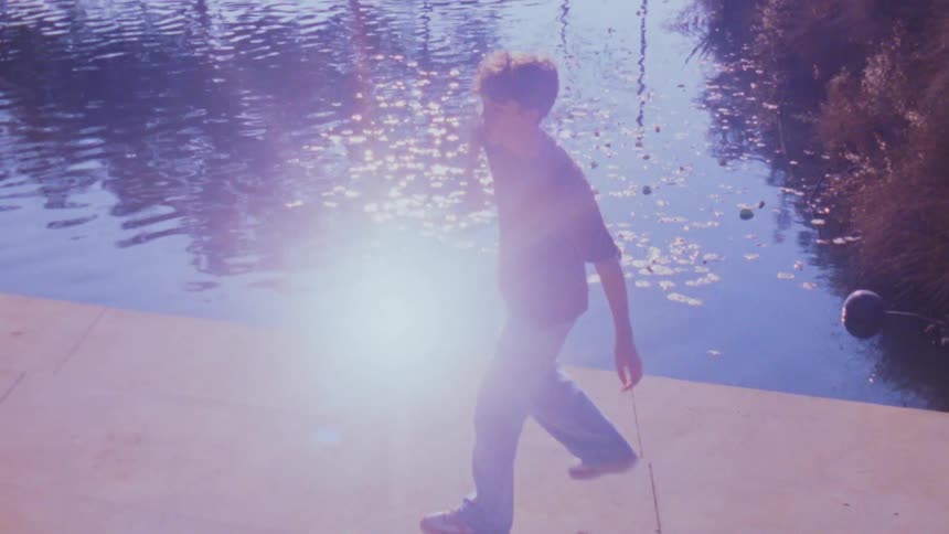 A teenage male dancer dancing outdoors by a pond during daytime
