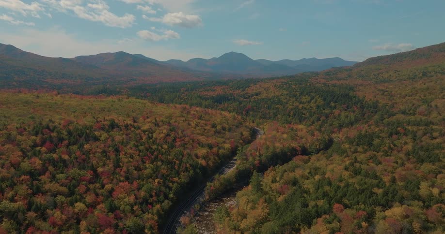 Traffic moves on a highway through forested mountains with trees in bright fall colors