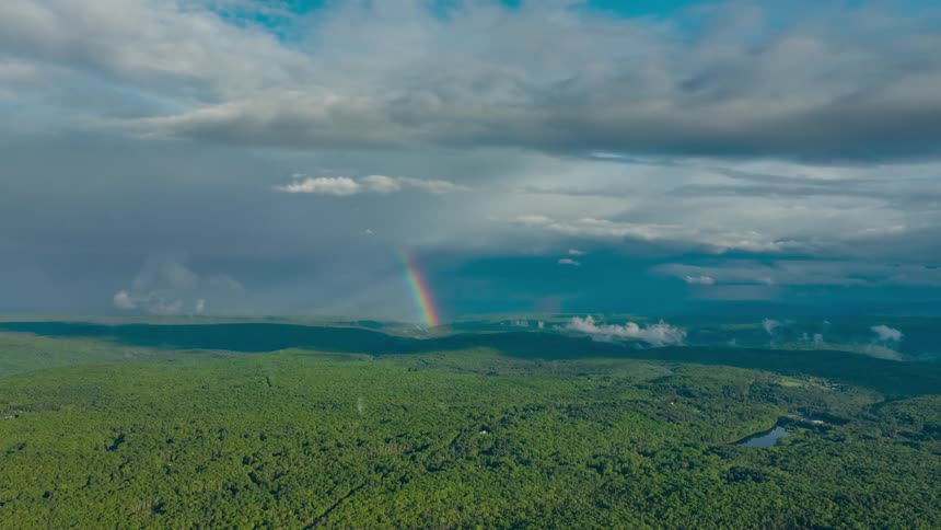 The clouds are moving across the forest and you can see the shadows moving across the forest below and there is a rainbow in the background