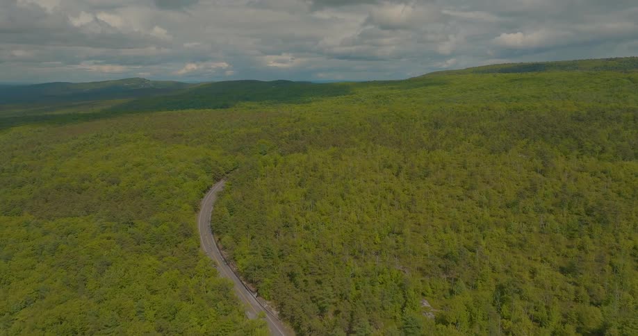 Narrow road winds through a vast forested area under a partly cloudy sky