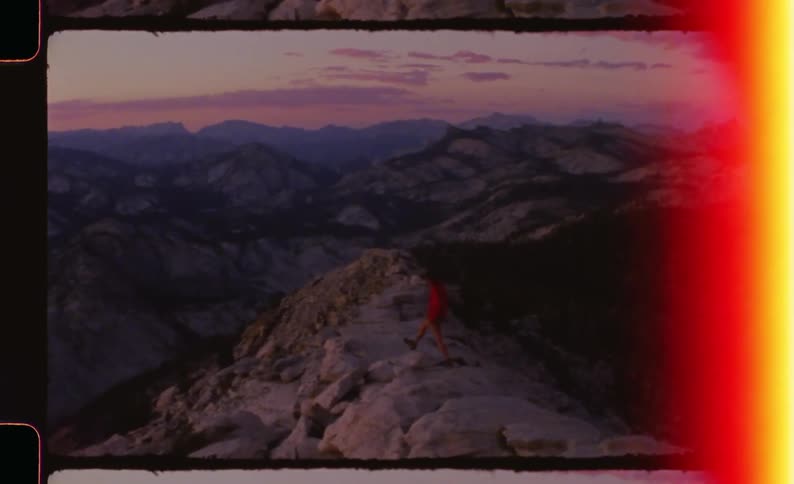 Hiker dressed in red walking around rocks on a mountain with valleys and other mountains on the background outdoors during dusk or dawn