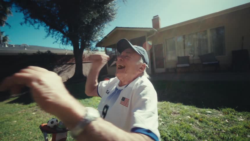 Elderly man sits in his backyard watching something on his smartphone