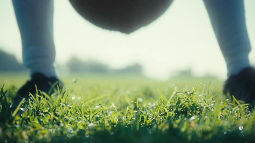Person walking and positioning a soccer ball on a grass field