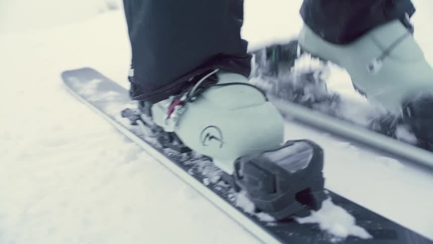 Skier steps into their skis as they stand on the snow