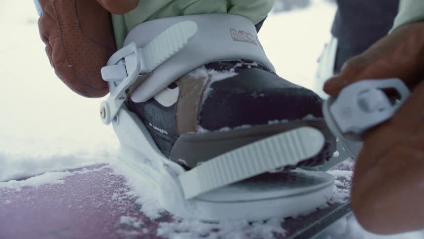 Snowboarder strapping on their snowboard as they stand on the snow