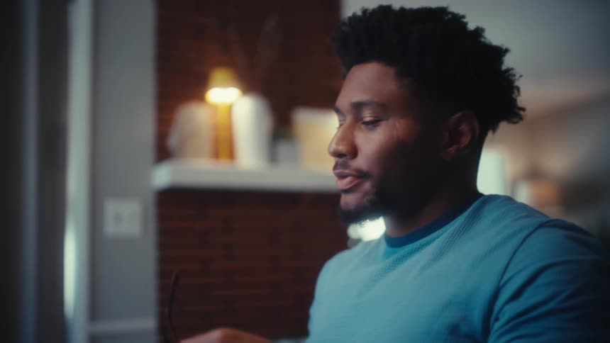 A man in a blue shirt reacts with a mixture of excitement and frustration before putting on his glasses he then leans back and looks upward appearing to process a moment of intense emotion or reflection