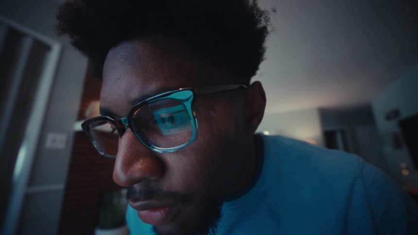 A young man working at his laptop leans in close to the screen with a look of surprise and excitement