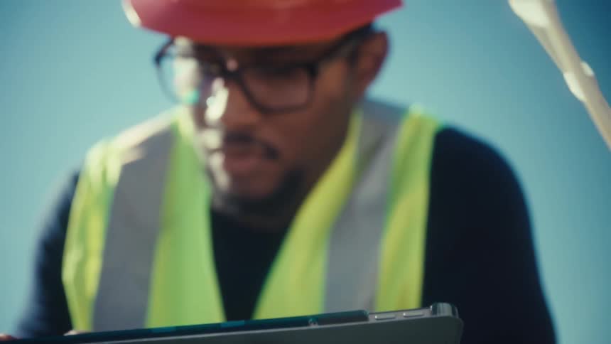 Worker wearing a safety vest uses a tablet while outdoors during the daytime