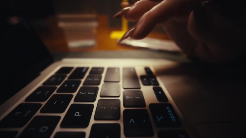 A persons finger presses the keys of a computer keyboard a gold ring shining on her finger as she types