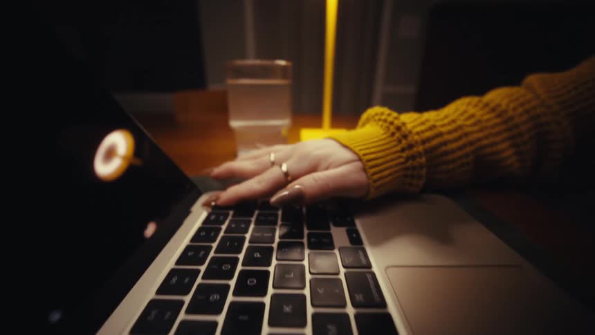 Woman with long painted fingernails opens her laptop while sitting at home at night