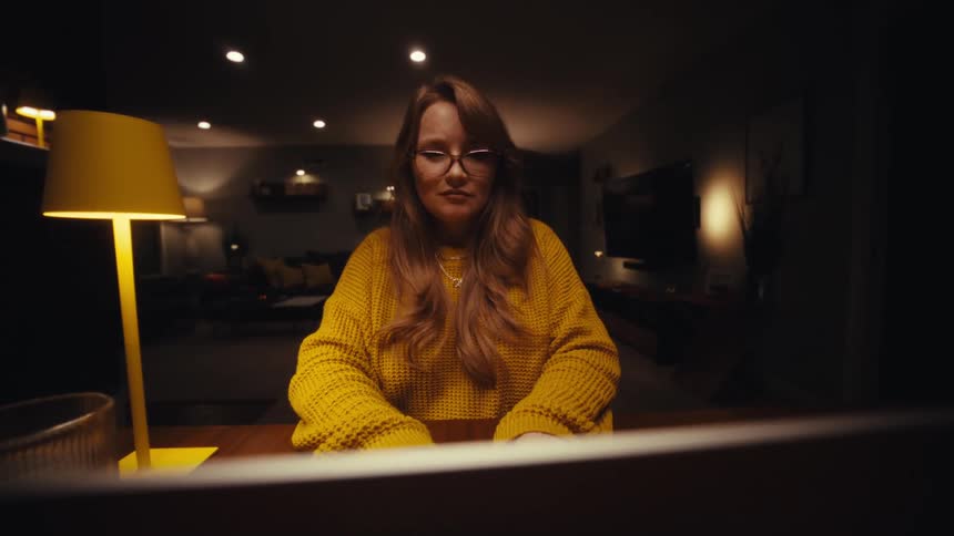 A woman in a bright yellow sweater opens her laptop at a dark table and begins typing