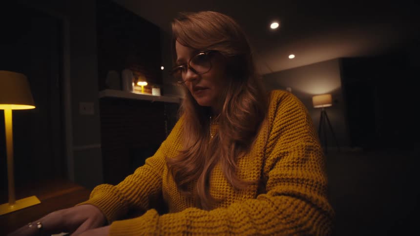 A woman opens her laptop and begins typing smiling briefly