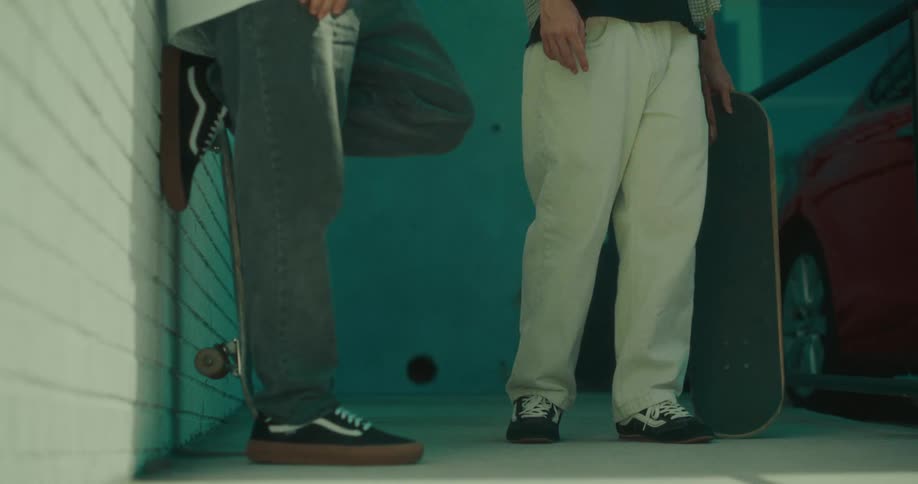 Two skateboarders stand with their boards against a teal wall and white brick corner