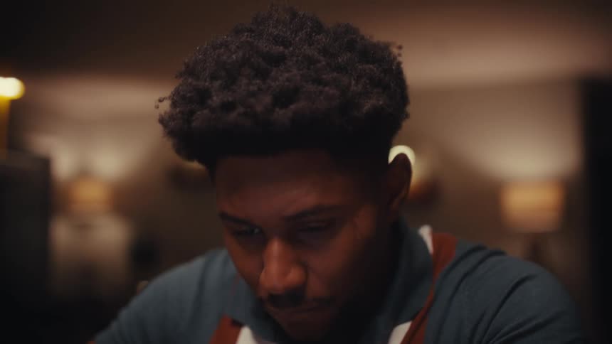 Close up of a young black man using a tablet computer while sitting at a table indoors at night