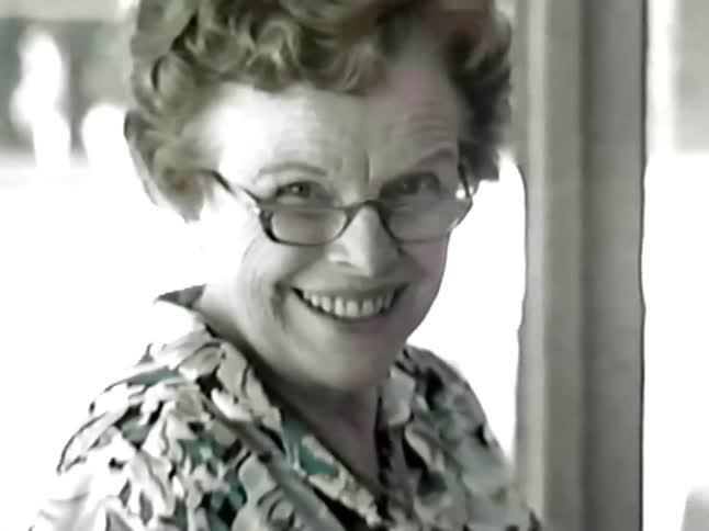 An elderly woman laughing while having a conversation with another person indoor
