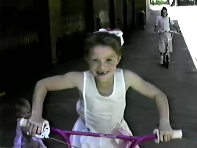 The girls ride their bicycles past the building