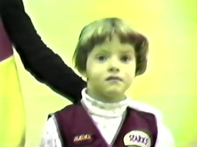 Young girl standing next to a person in a mascot costume waving and smiling in a room with many other people passing by