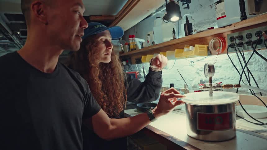 Two people are examining a device on the bench