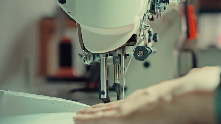A fashion designer stitches fabric with a sewing machine a wristwatch visible on their arm as they work with steady precision