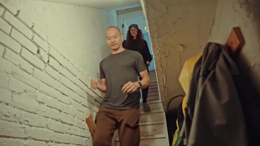 A man and a woman walking down a narrow whitewalled staircase into a basement or lowerlevel room