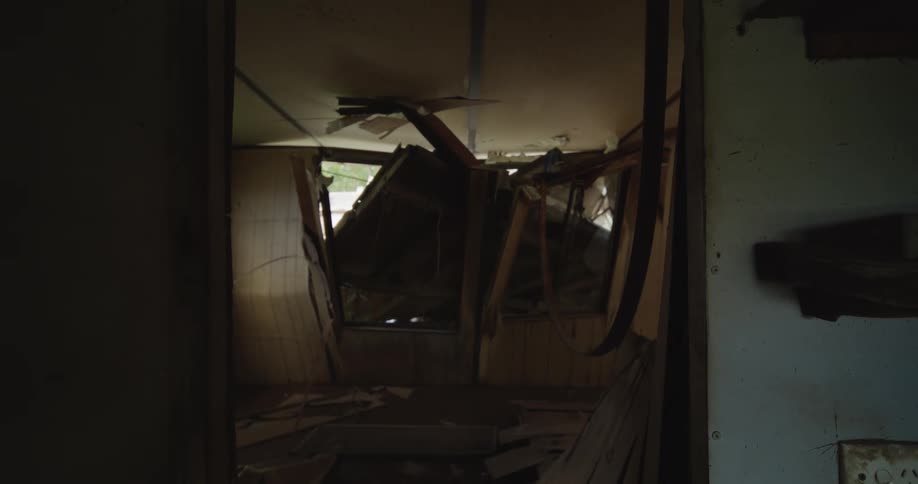 View through a doorway into a destroyed room with a collapsed ceiling and wooden debris scattered across the floor