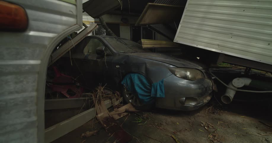 A scrap car sits parked inside a garage its body covered with scattered metal pieces and other discarded parts