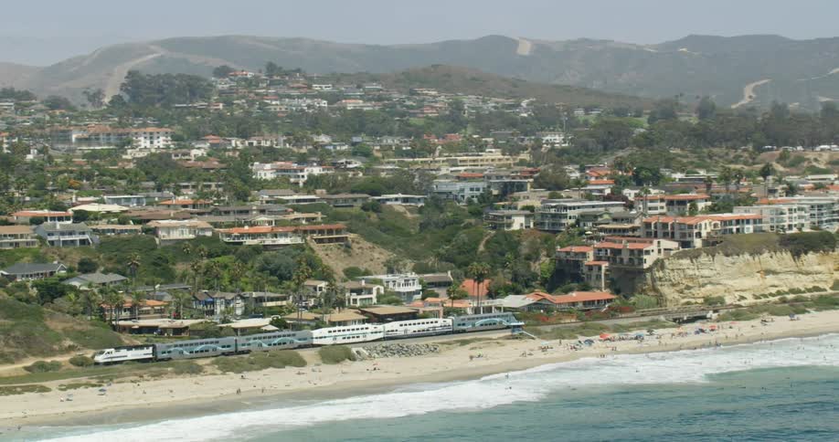 A train travels on the coast near buildings and homes in San Diego, California