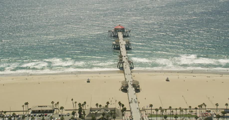 Huntington Beach with palm trees, a long pier and cars parked in a parking lot