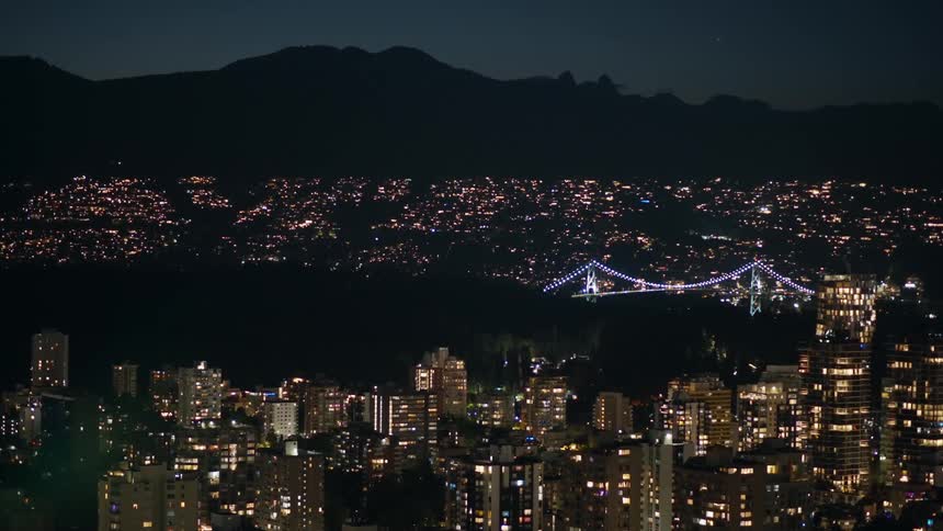 A large city lit up at night with a distant bridge and mountainscape
