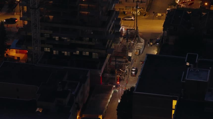 The camera is looking down on the city and there are flashing red and blue lights cars parked and moving on the streets and people walking on the streets