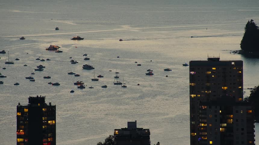 A city skyline at sunset with an ocean view in the background filled with boats