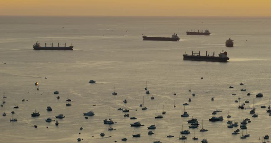 Cargo ships and smaller vessels anchored in a coastal area at dusk