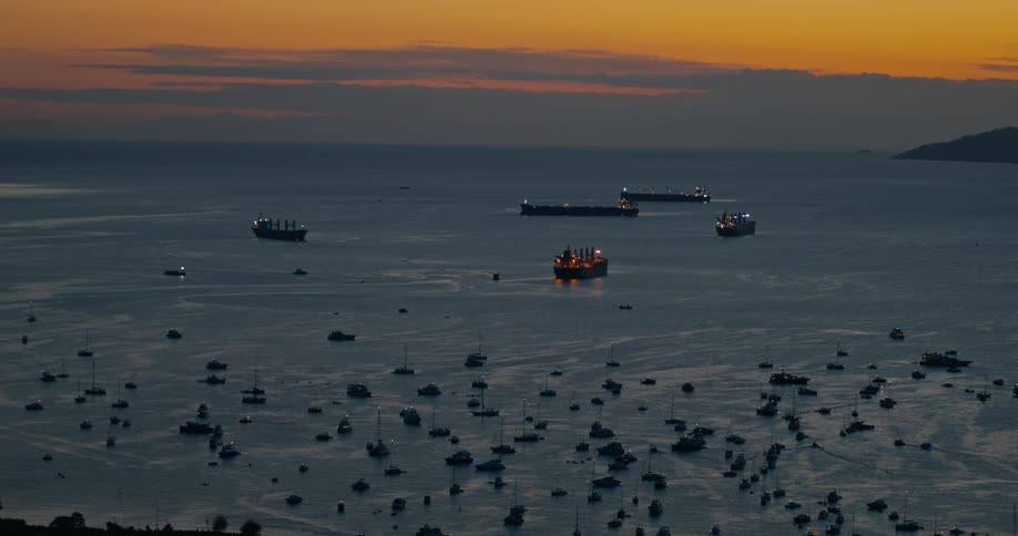 Small boats and lit cargo ships scattered across waters at sunset