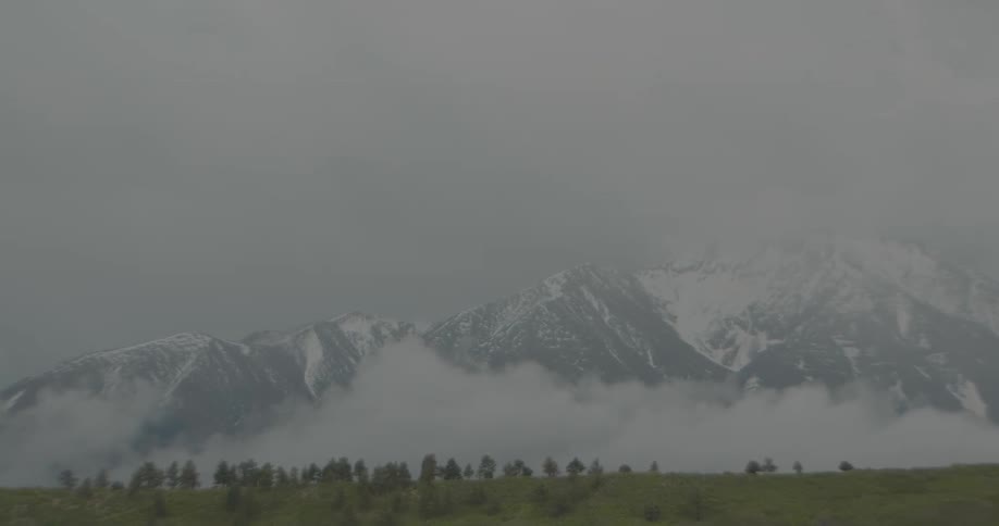Mist over a mountain partially covered in ice next to a green field outdoors during day time