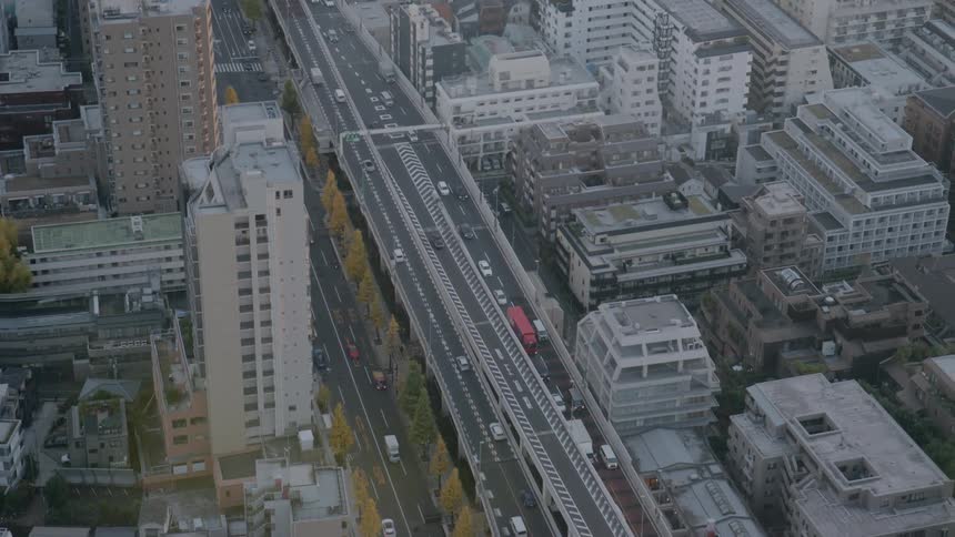 Highangle aerial footage captures steady traffic moving along a major multilane highway and surface roads winding through a dense residential and commercial district during a grey overcast day