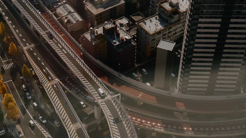 A busy city highway with a series of overhead bridges as cars drive by on a sunny day with highrises and skyscrapers lining the sides