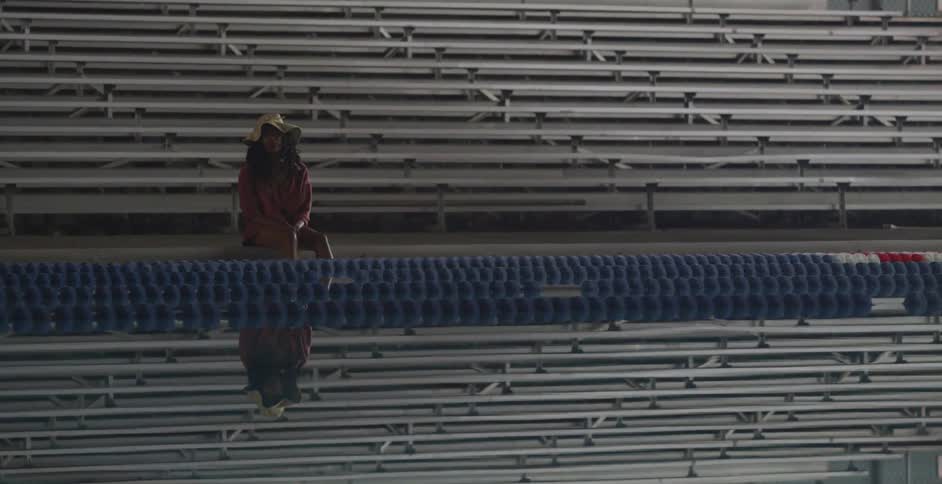 A woman sits in empty bleachers by a pool