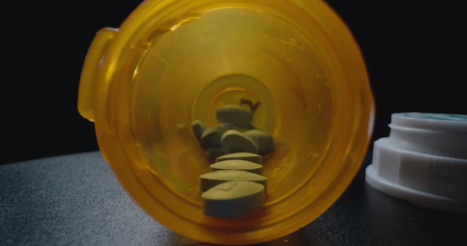 A small bottle of pills is open and multiple pills are spilled out