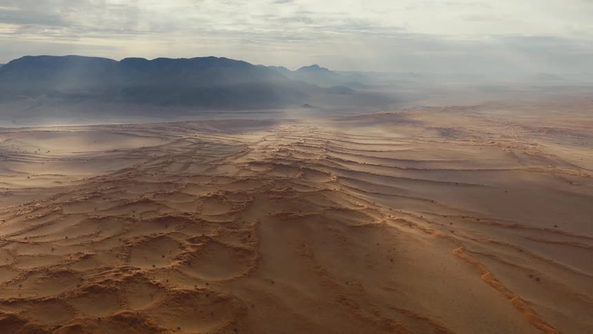 Desert dunes stretch toward faraway mountains under a cloudy dusk sky