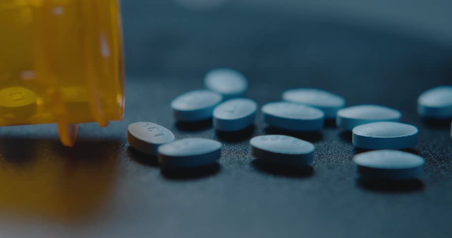 Blue medicine pills on a surface next to a plastic bottle indoors