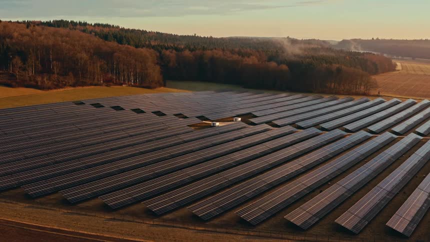 Solar farm with rows of photovoltaic panels installed in a rural area surrounded by forest