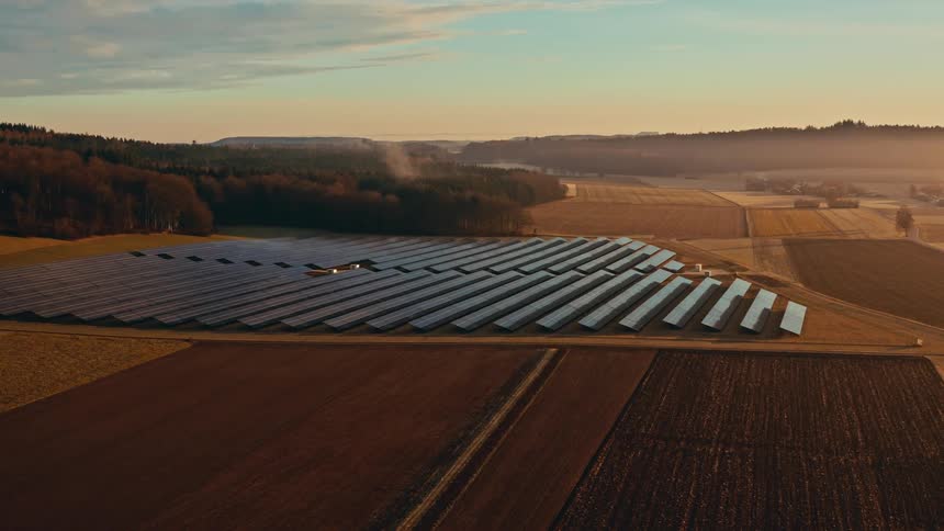 Solar plant on a field next to a forest with hills on the background outdoors during dusk or dawn