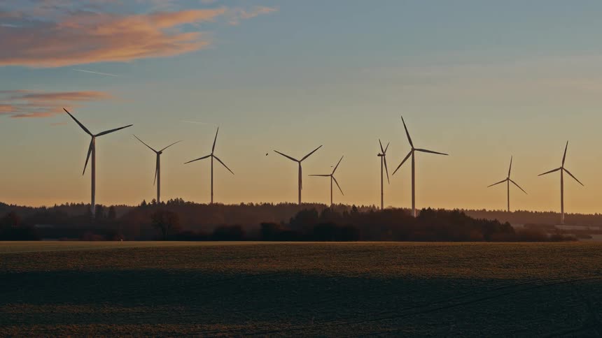 Several large wind turbines located near a forest spin in the wind
