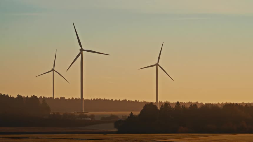 Turbines spin on a wind farm as traffic moves on the roads