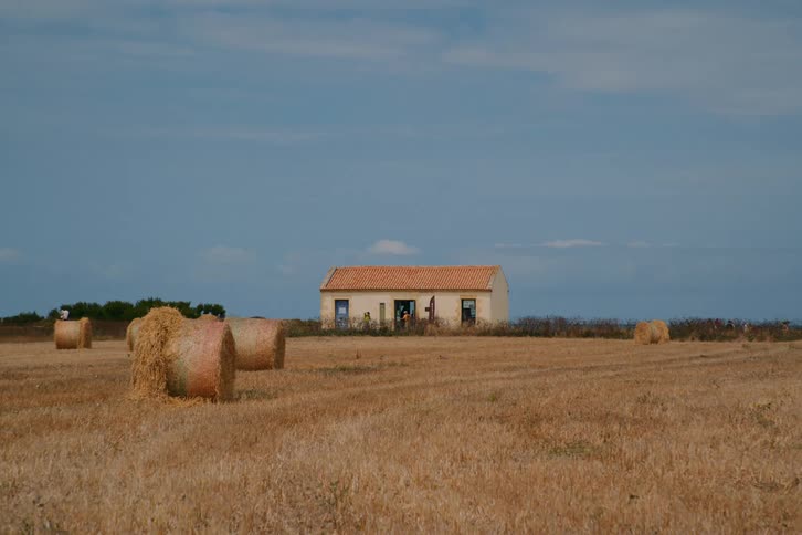 Isolated rural house in a dry field with hay bales scattered around
