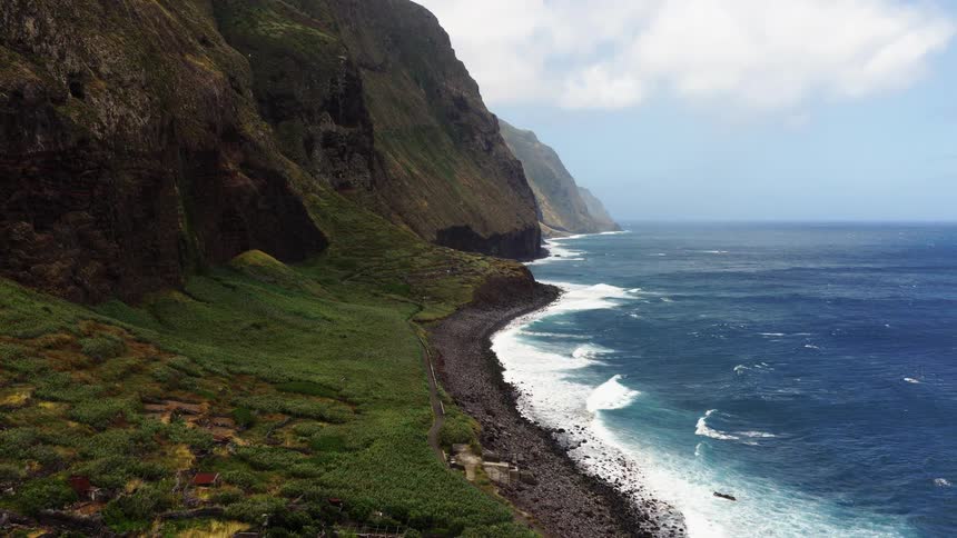 Aerial view of a green valley with small buildings nestled between cliffs by the ocean